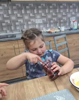 Dziewczynka wyjada dżem ze słoika.