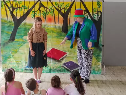 Dzieci siedzą na ławeczkach i oglądają przedstawienie teatralne.