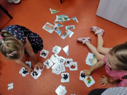 Dzieci układają puzzle na podłodze biblioteki.