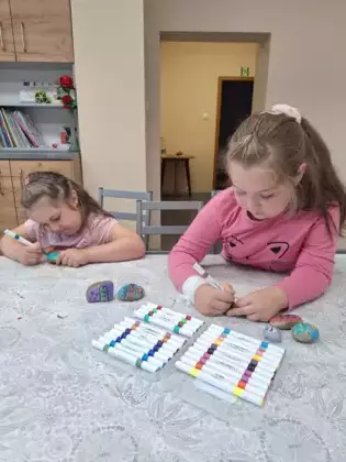 Dwie dziewczynki malują kamienie kolorowymi markerami.