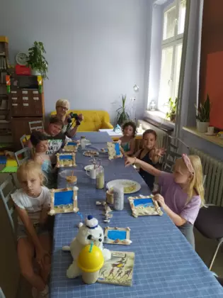 Dzieci siedzą przy stole i pokazują ramki zrobione na zajęciach.