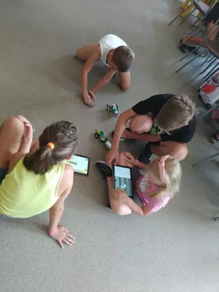 Dzieci siedzą na podłodzi i jeżdżą pojazdami z lego.