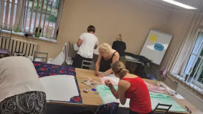 Uczestniczki warsztatów wycinają nożyczkami ubranie z materiału.