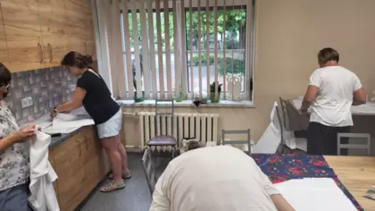 Uczestniczki warsztatów wycinają nożyczkami ubranie z materiału.