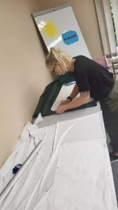 Uczestniczka warsztatów wycina nożyczkami ubranie z materiału.