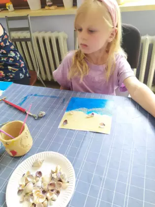 Dziewczynka przykleja muszelki do obrazka.