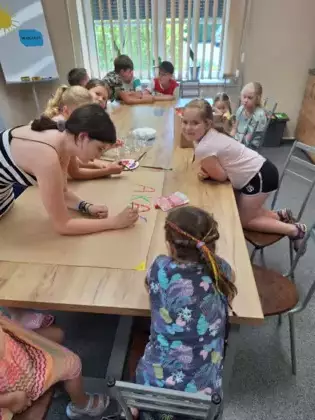 Uczestnicy zajęć malują duży plakat farbami.