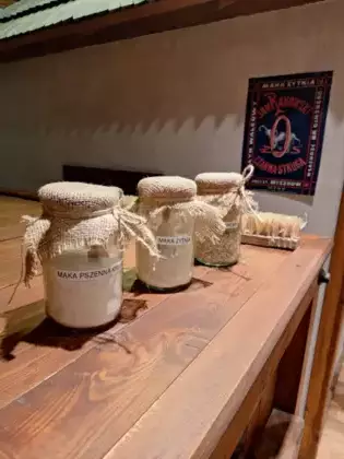 Na półce stoją trzy słoiki z mąką obok leży szczotka.