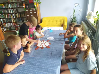 Dzieci farbami malują ster statku.