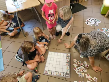 Pani prowadząca zajęcia tłumaczy dzieciom, w jaki sposób wykonać zadanie, które mają przed sobą na macie do kodowania.