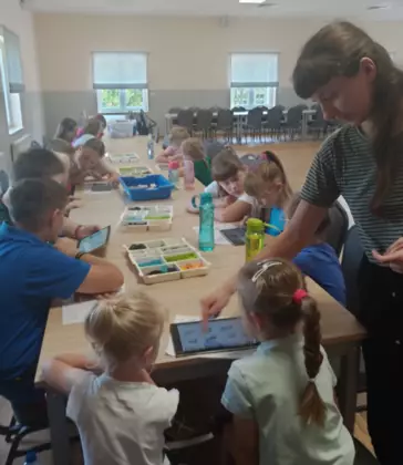 Pani prowadząca zajęcia objaśnia w jaki sposób połączyć klocki lego, aby można było nimi sterować za pomocą tableta.