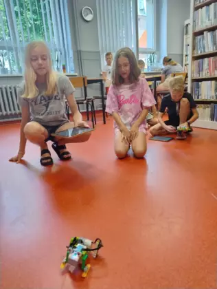 Uczestnicy jeżdżą zbudowanymi pojazdami po bibliotece.