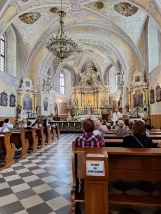 Uczestnicy wycieczki siedzą w ławkach w sanktuarium Matki Boskiej Leśniewskiej.