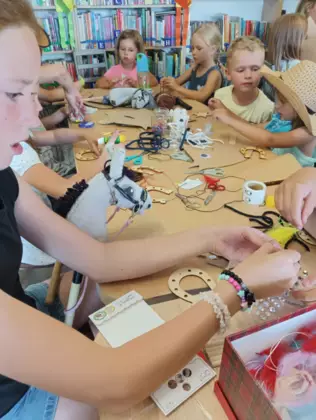 Dzieci siedzą przy stoliku i wykonują prace plastyczne.