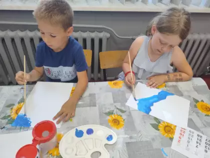 Dziewczynka i chłopczyk malują farbami wakacyjne obrazki.