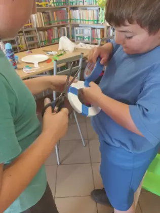 Chłopcy oklejają koło ratunkowe niebieską taśmą.