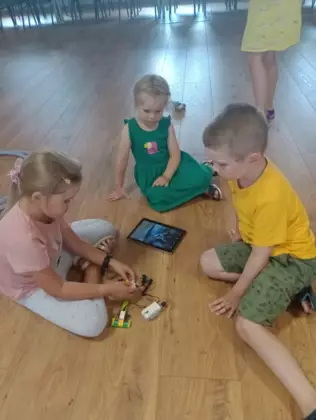 Dzieci dokonują poprawek w swoich klockowych maszynach jeżdżących.