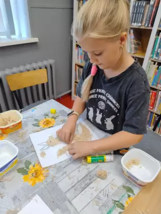 Dziewczynka przykleja kawałki wełny do obrazka kangurka.