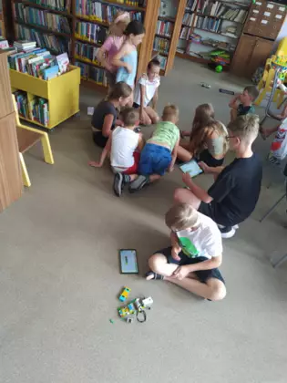 Dzieci siedzą na podłodzi i jeżdżą pojazdami z lego.