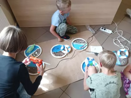 Dzieci przyklejaja muszelki i koła ratunkowe do swoich prac wakacyjnych.