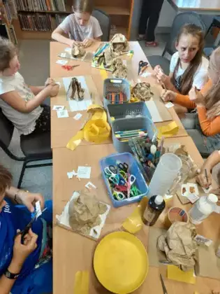 Dzieci siedzą przy stoliku i wykonują prace plastyczną.