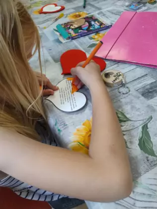 Dziewczynka na serduszku pisze życzenia dla taty.