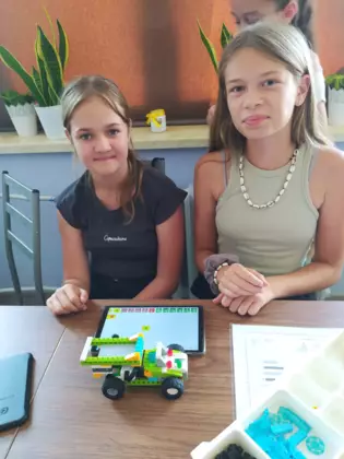 Dziewczyny prezentują pojazd złożony z klocków.