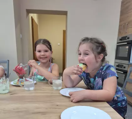 Dziewczynki jedzą jagodzianki upieczone na warsztatach.