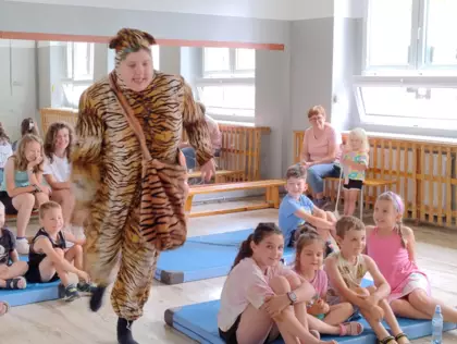 Dzieci siedzą na ławeczkach i oglądają przedstawienie teatralne.