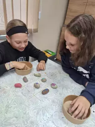 Uczestniczki zajęć grają w grę kółko krzyżyk zrobioną z pomalowanych kamyczków.