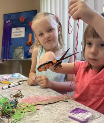Dziewczynka obcina nożyczkami kolorową włóczkę.
