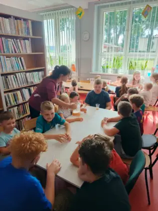 Prowadząca nalewa sok do kubeczków dzieciom siedzącym przy stoliku.