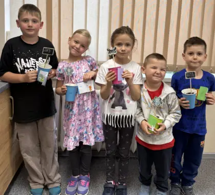 Pięć uśmiechniętych dzieci z kubeczkami w ręce i małymi książeczkami.