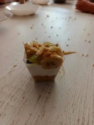 Deserek w pojemniczku składający się z granoli, jogurtu, owoców i kruszonki.