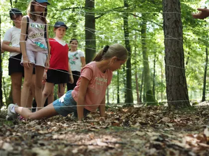 Kilkunastoletnia dziewczynka przechodzi w lesie pod zamocowanym sznurkiem do pni drzew.