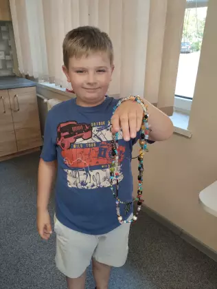 Chłopiec trzyma w ręce kolorowy naszyjnik z koralików.