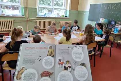 Dzieci siedzą przy wspólnym stole i słuchają bajki.