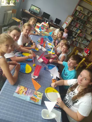 Dzieci siedzą przy stole i malują farbami morze.