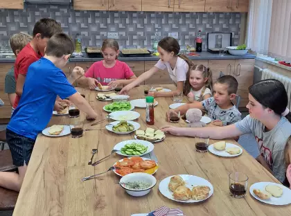 Dzieci przy wspólnym stole przygotowują hamburgery.