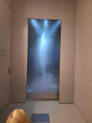 W prostokątnej wnęce, oświetlonej trzema lampami, widać małą trąbę powietrzną.