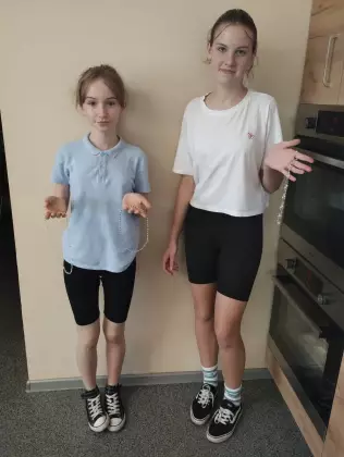 Dwie dziewczyny pokazują zrobioną przez siebie kolorowe naszyjniki i bransoletki.