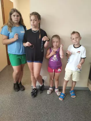 Czworo dzieci stoi koło siebie i trzyma w rękach zrobioną przez siebie biżuterę z kolorowych koralików.