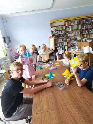 Dzieci siedzą przy wspólnym stole i wykonują prace plastyczne metodą origami.