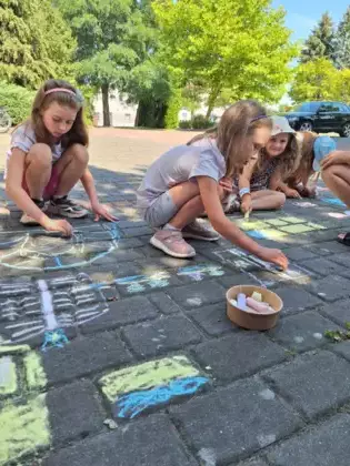 Dzieci maliją kolorową kreda obrazki na chodniku przed biblioteką.