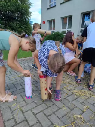 Dzieci wkładają do pomalowanych tub siano i szyszki tworząc domki dla owadów.
