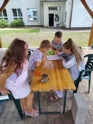 Dzieci pisza notatkę o złapanych owadach, które trzymają w pojemniku.