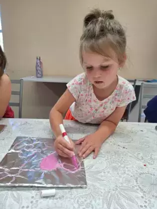 Dziewczynka maluje różowe serduszko na folii  aluminiowej.