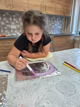 Dziewczynka maluje kolorową tęczę na folii aluminiowej.