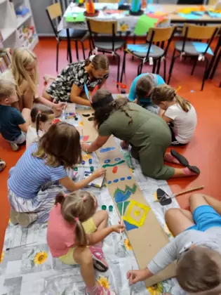 Dzieci na podłodze malują farbami duży posąg wodza indiańskiego wykonany z tektury.