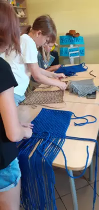 Uczestniczki warsztatów pletą kolorowe torebki stylem makramy.